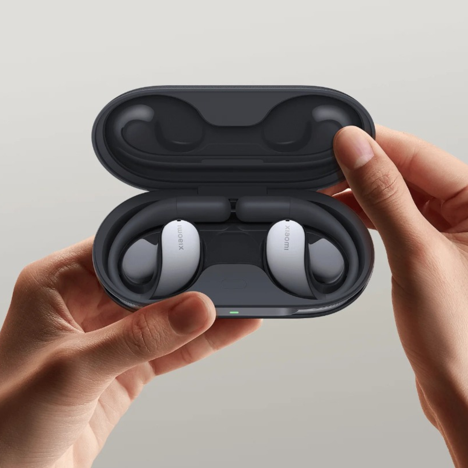 A pair of Xiaomi Open Wear Stereo Earbuds in a charging case, held in a person's hands.