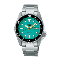 A Seiko SRPK33K1 watch with a turquoise dial, silver stainless steel bracelet, and a black casing. The watch has a round shape and displays features such as day-date indication and luminous hands.