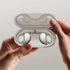 Wireless earbuds in a white case held by hands against a plain background.